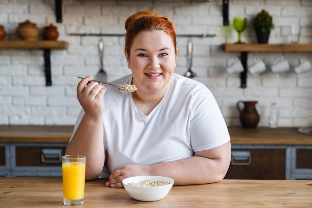 Happy caucasian fat obese plump woman eating flakes for healthy eating habits.